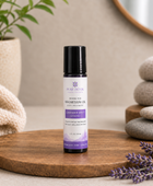 A 1 oz bottle of Pure Intox Magnesium Oil body treatment stands on a round wooden tray, styled with lavender sprigs, stacked stones, and a folded cream textile in a warm neutral setting.