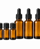 Six amber glass dropper bottles of different sizes with black rubber droppers and black ribbed caps, arranged by size on a white background.