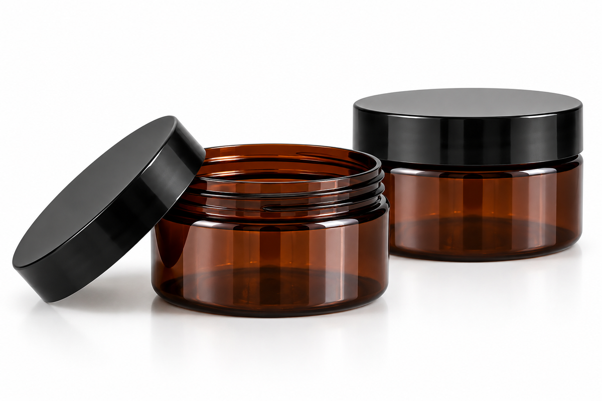 Two empty amber PET cosmetic jars with black screw-on lids on a clean white background, with one jar open and its lid leaning against it.