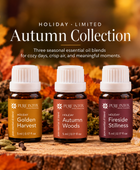 Three Pure Intox essential oil bottles from the Holiday Limited Autumn Collection are displayed on a rustic wood slice surrounded by autumn leaves, orange slices, cinnamon, and a candle. The bottles are labeled Golden Harvest, Autumn Woods, and Fireside Stillness.