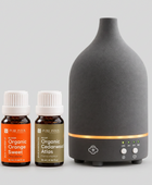 A matte black ceramic diffuser with a glowing orange LED band and two small Pure Inton essential oil bottles on a clean white background.