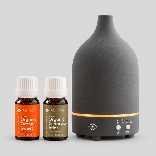 A matte black ceramic diffuser with a glowing orange LED band and two small Pure Inton essential oil bottles on a clean white background.