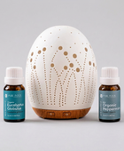A white ceramic diffuser with laser-cut geometric patterns and a wooden base, flanked by two Pure Inton essential oil bottles labeled Organic Eucalyptus Globulus and Organic Peppermint on a white background.
