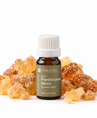 A 5 mL bottle of Pure Intox Root Frankincense Sacra essential oil, surrounded by golden amber resin crystals on a clean white background.