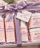 A gift set of Pure Intox skincare products in a white box tied with a lavender ribbon. The set includes four pump bottles and three cream jars in soft pink and white packaging, arranged in shredded purple filler with a small gift tag reading 'A More Radiant You'