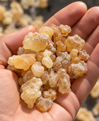 A close-up of a hand holding a pile of translucent, amber-colored natural resin or gum pieces, with more pieces blurred in the background.