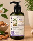 A bottle of Pure Intox Sweet Almond Oil Organic in a dark green glass bottle with a black pump, styled on a wooden table with almonds, white blossoms, and a beige knit blanket.