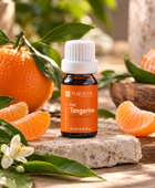 A bottle of Pure intox Rise Tangerine citrus essential oil placed on a stone slab, surrounded by fresh oranges, orange slices, green leaves, and a white tangerine blossom in a warm, natural setting.