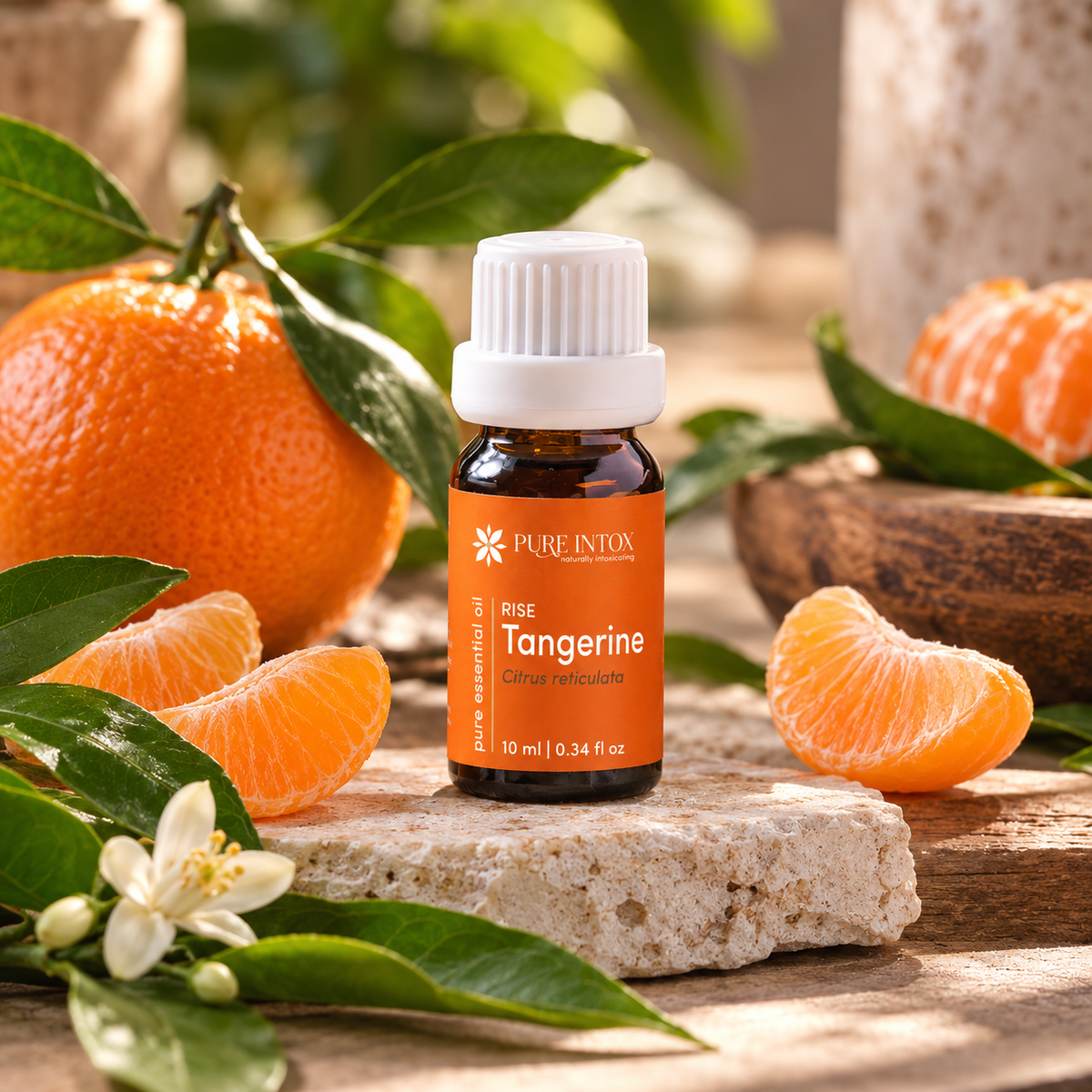 A bottle of Pure intox Rise Tangerine citrus essential oil placed on a stone slab, surrounded by fresh oranges, orange slices, green leaves, and a white tangerine blossom in a warm, natural setting.